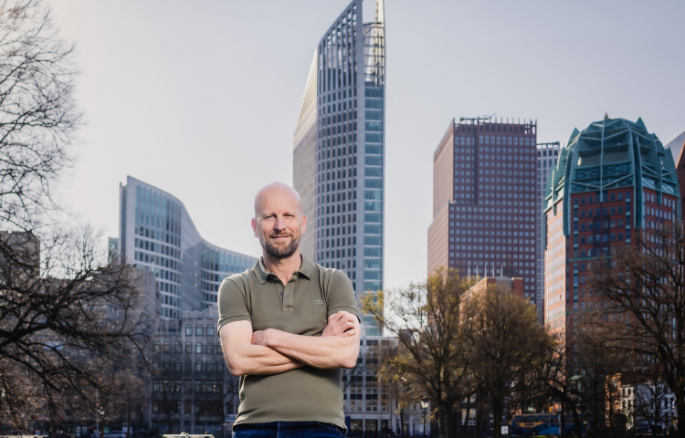 Projectmanager leefomgeving Stephan staat met armen over elkaar en kijkt in de camera. Op de achtergrond de skyline van Den Haag.